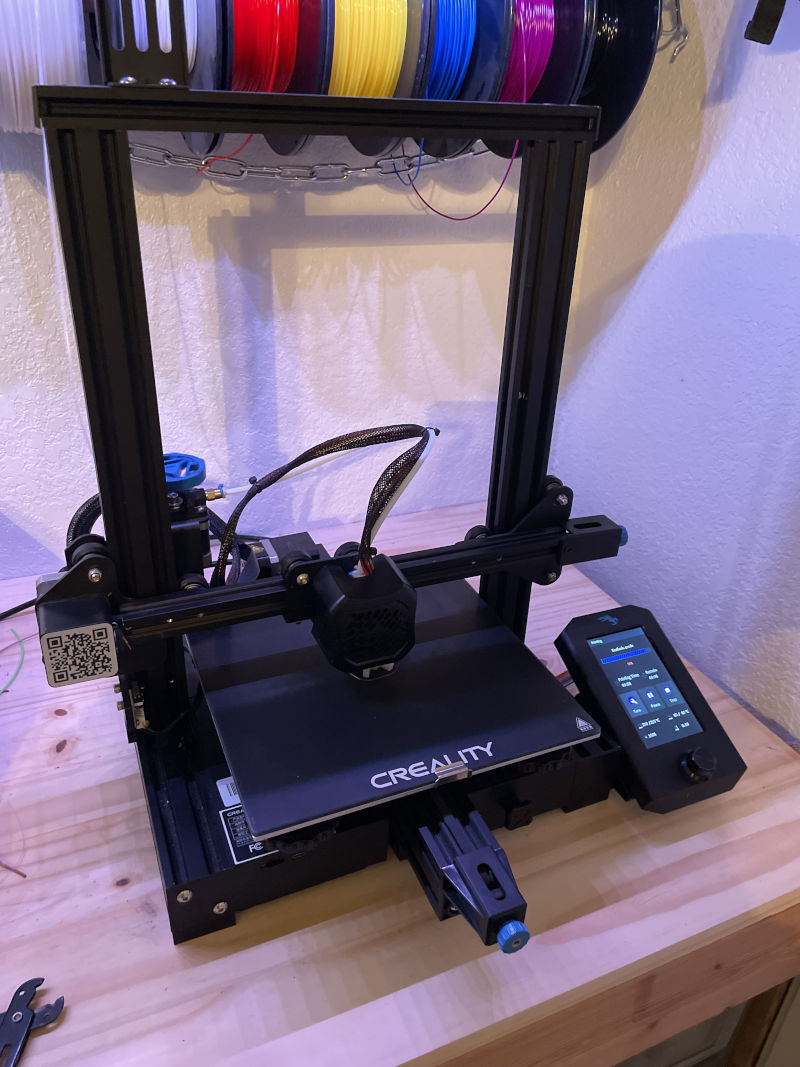 A Creality Ender 3 v2 on a desk with filament rolls hanging behind it.